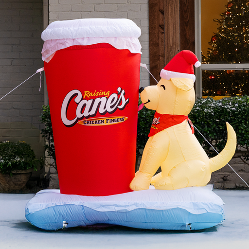 Inflatable Raising Cane's lemonade cup with a dog wearing a Santa hat in front of a house.