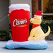 Inflatable Raising Cane's lemonade cup with a dog wearing a Santa hat in front of a house.