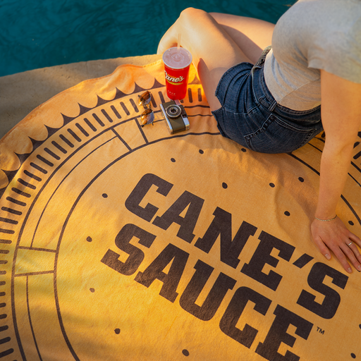 Person sitting on a Cane's Sauce beach towel by a pool