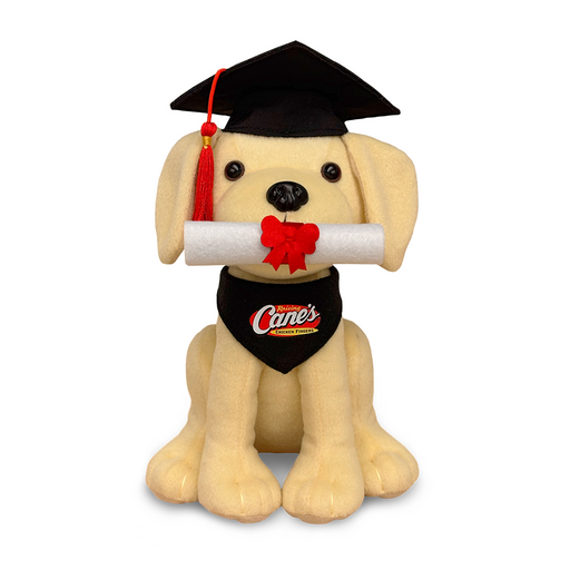 A plush toy of a yellow puppy wearing a black graduation cap and a Raising Cane's black bandana, holding a red and white diploma in its mouth.