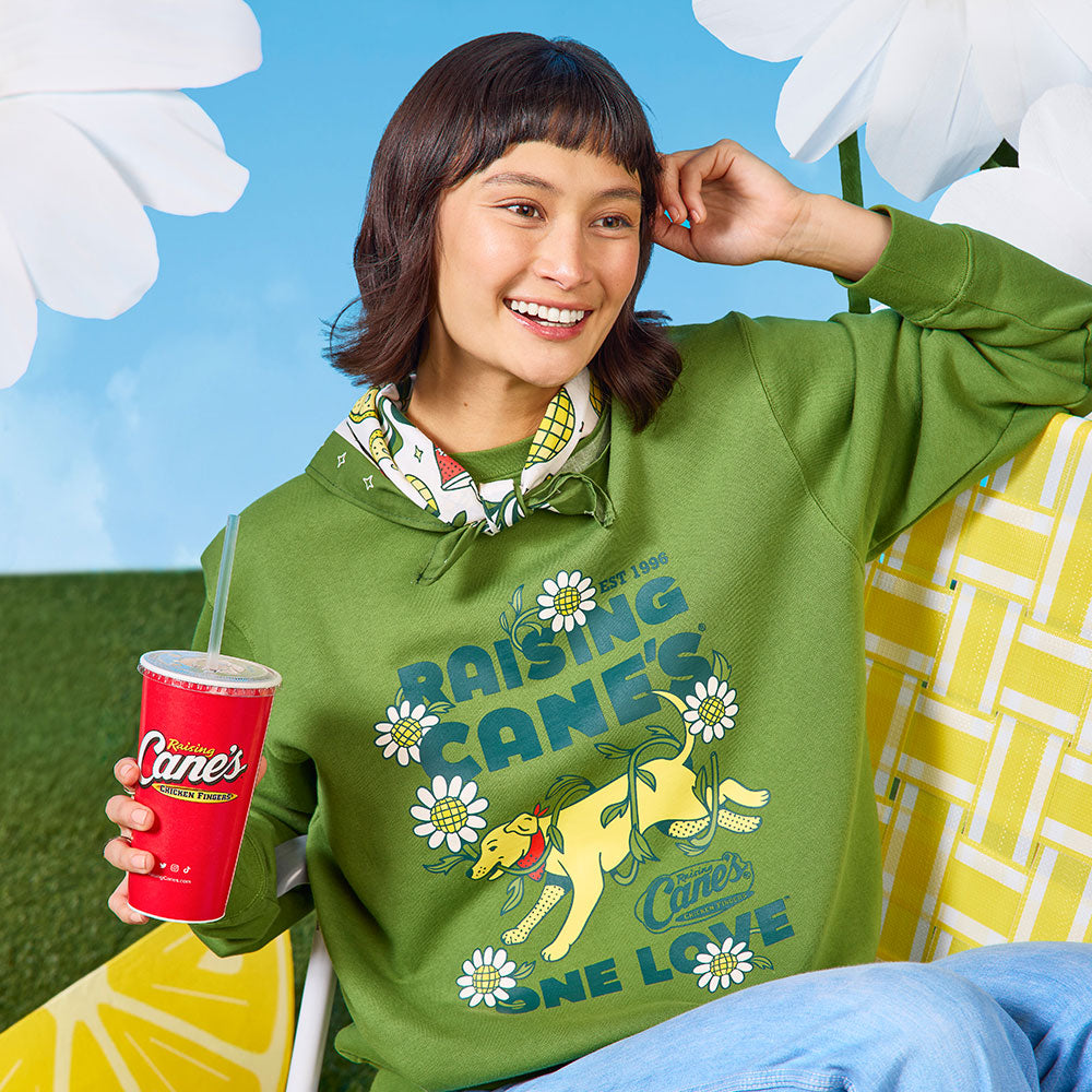 Person wearing a green hoodie with Raising Cane's logo, holding a red cup, against a bright background