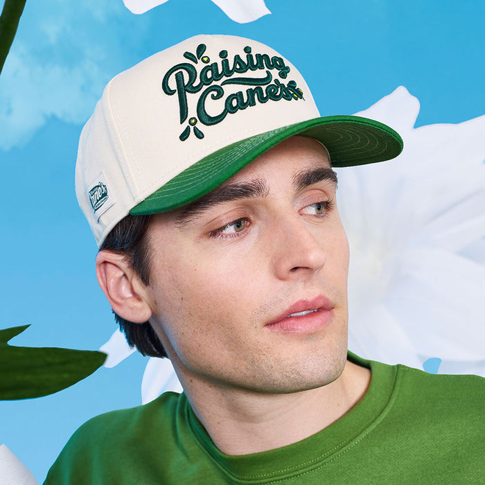 Model wearing a Raising Cane's cap against a blue sky and cloud background 