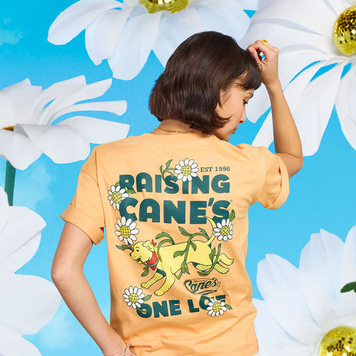 Woman model wearing the Cane III Floral Tee, a yellow T-shirt with Raising Cane’s branding, posed against a floral background