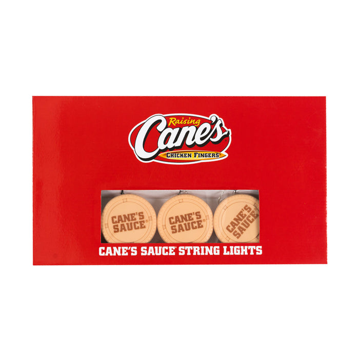 Raising Cane's Chicken Fingers sauce packaging with string lights on a red background
